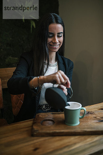 Porträt einer jungen Frau in einem Café  die Tee in eine Tasse gießt