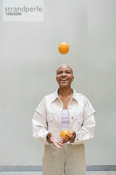 Glückliche Frau jongliert im Freien mit Orangen