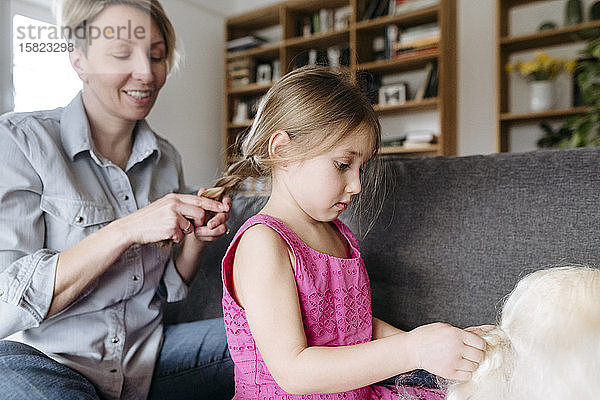 Mutter flechtet das Haar ihrer Tochter auf der Couch