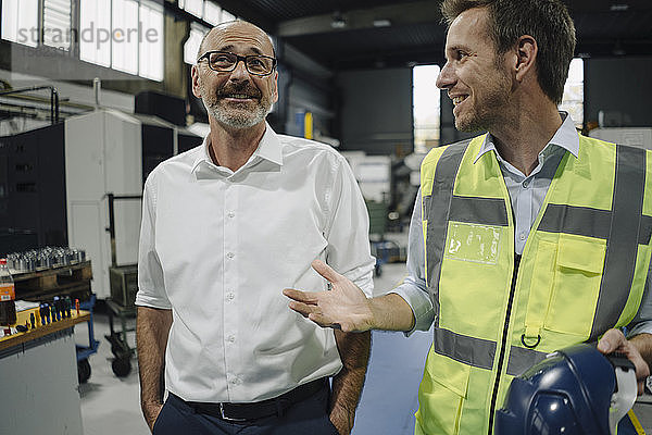 Geschäftsmann und Mann in reflektierender Weste im Gespräch in einer Fabrik