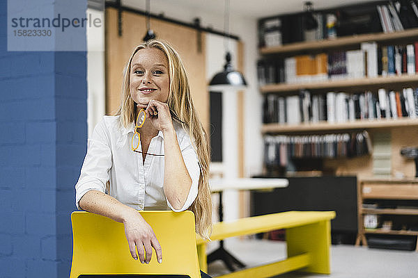 Porträt einer lächelnden jungen Geschäftsfrau  die auf einem Stuhl im Loft-Büro sitzt