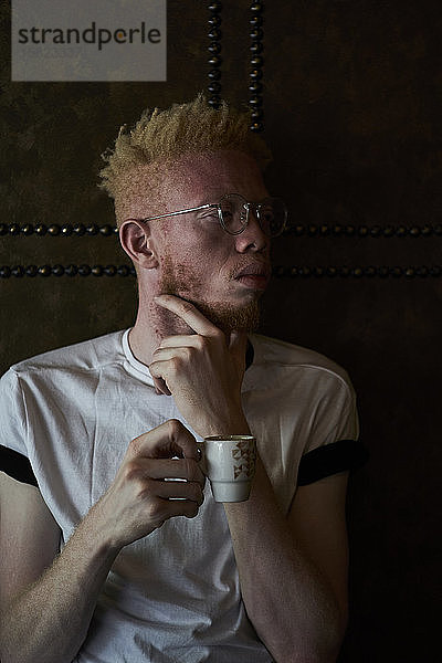 Albinomann hält eine Tasse Kaffee und schaut zur Seite