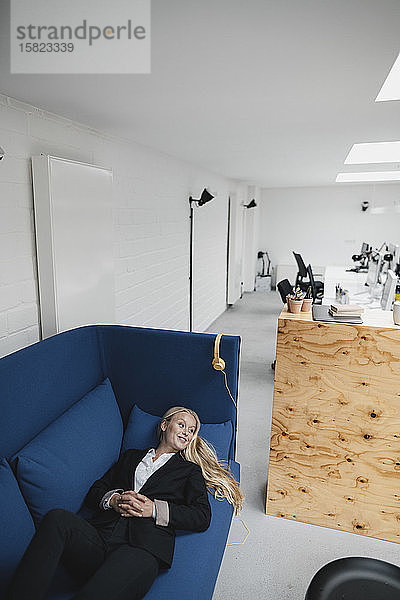 Lächelnde junge Geschäftsfrau liegt im Büro auf der Couch