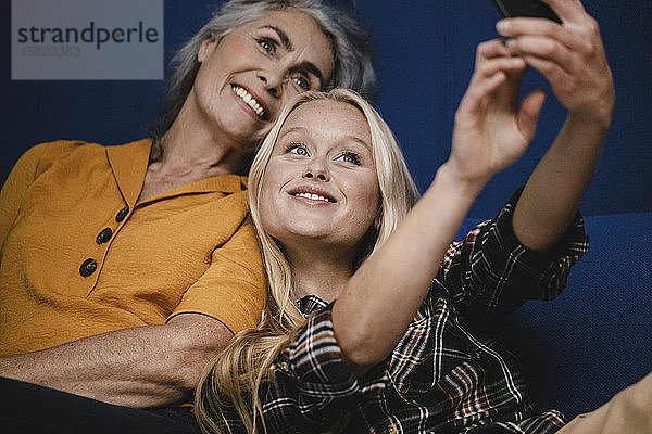 Glückliche Mutter und erwachsene Tochter  die auf der Couch ein Selfie machen