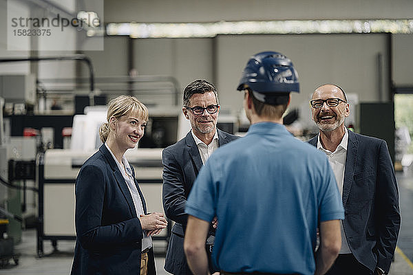 Lächelnde Geschäftsleute sehen Arbeiter in einer Fabrik an