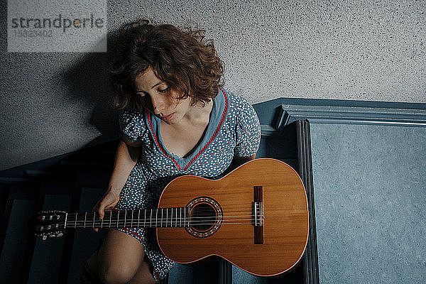 Traurige junge Frau sitzt mit Gitarre auf der Treppe