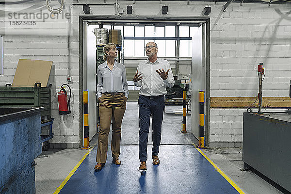 Mann und Frau gehen und sprechen in einer Fabrik