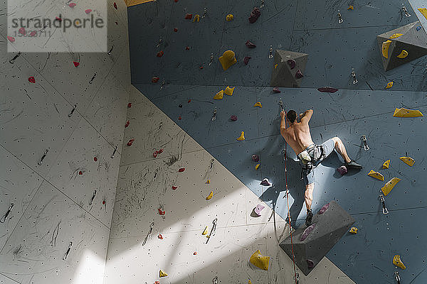 Mann ohne Hemd klettert in Kletterhalle an der Wand