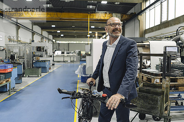 Lächelnder Geschäftsmann mit Fahrrad in einer Fabrik
