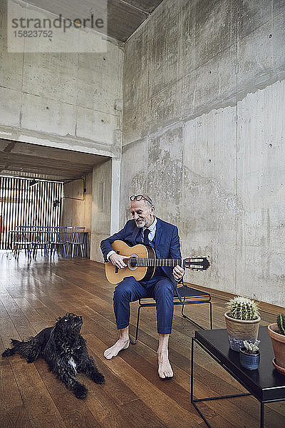 Leitender Geschäftsmann sitzt im Büro und spielt Gitarre für seinen Hund