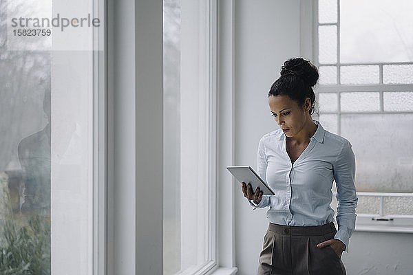 Erfolgreiche Geschäftsfrau  am Fenster stehend  mit digitalem Tablet  lesend