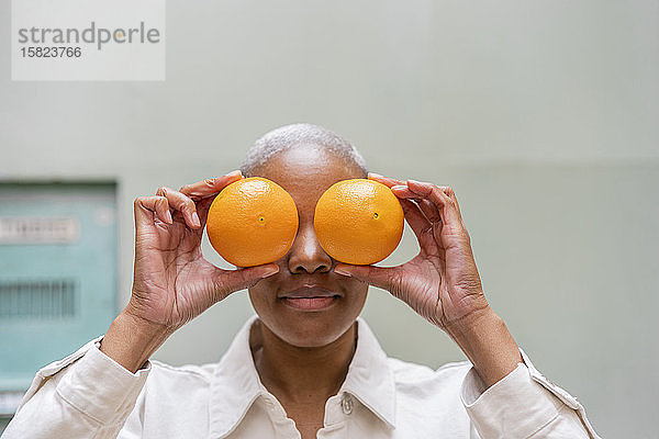 Frau bedeckt ihre Augen im Freien mit Orangen