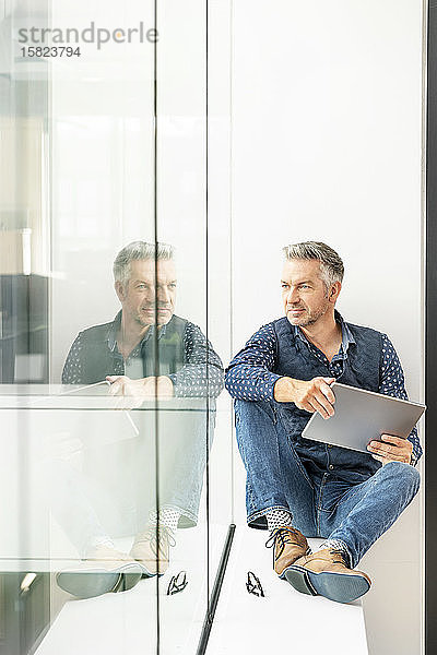 Gelegenheits-Geschäftsmann sitzt auf der Fensterbank eines Bürogebäudes und benutzt Laptp