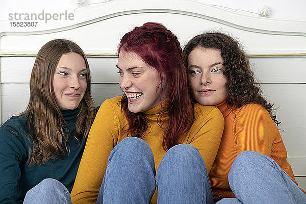 Porträt von drei glücklichen Schwestern  die zusammen auf dem Bett sitzen