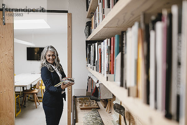 Lächelnde grauhaarige Geschäftsfrau hält Farbmuster in einem Loft-Büro