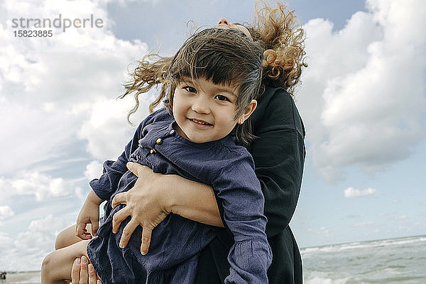 Porträt eines glücklichen kleinen Mädchens auf den Armen seiner Mutter