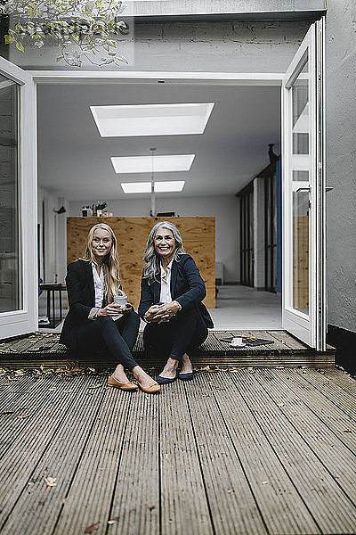 Lächelnde reife und junge Geschäftsfrau sitzt auf Holzterrasse