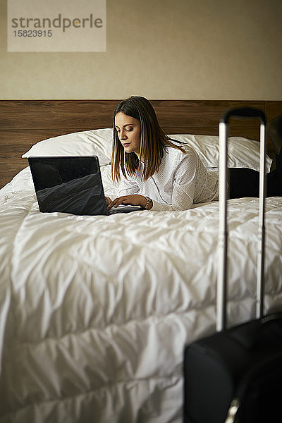 Geschäftsfrau  die im Hotelzimmer auf dem Bett liegt und einen Laptop benutzt