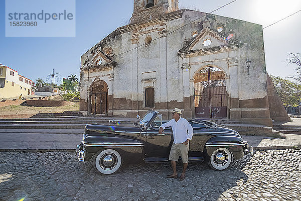 Taxifahrer  der neben einem Oldtimer-Cabriolet steht  Trinidad  Kuba