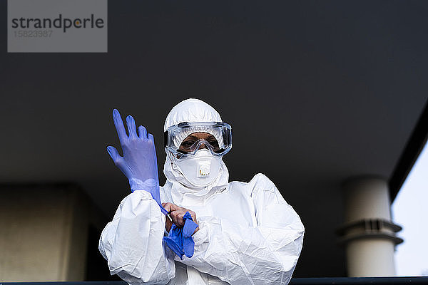 Wissenschaftlerin  die Schutzanzug und Maske trägt und Schutzhandschuhe anzieht