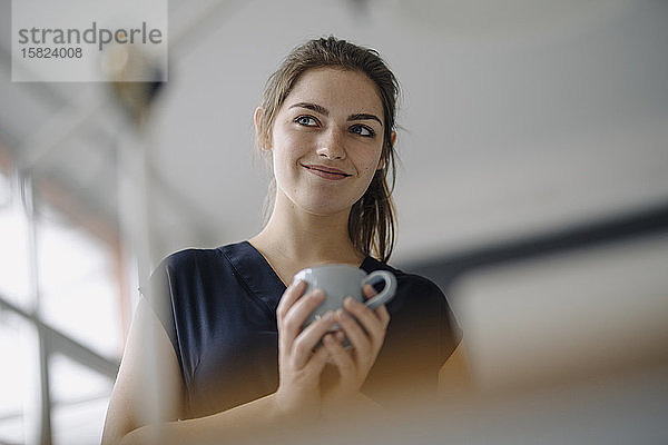 Porträt einer lächelnden jungen Frau mit einer Tasse Kaffee im Büro