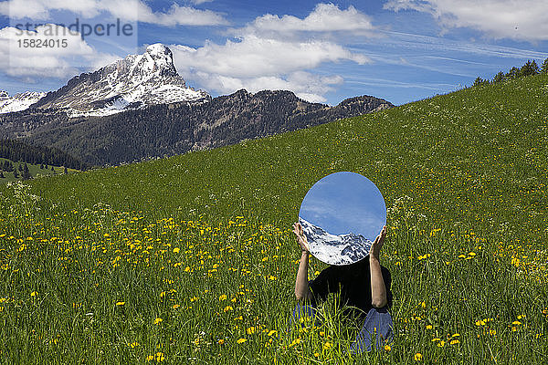 Frau sitzt auf einer Wiese  hinter einem Spiegel versteckt  in dem sich die Berge des Gadertals spiegeln  Südtirol  Italien