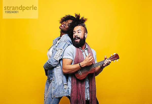 Glücklicher junger Mann mit Frau im Studio beim Ukulele spielen