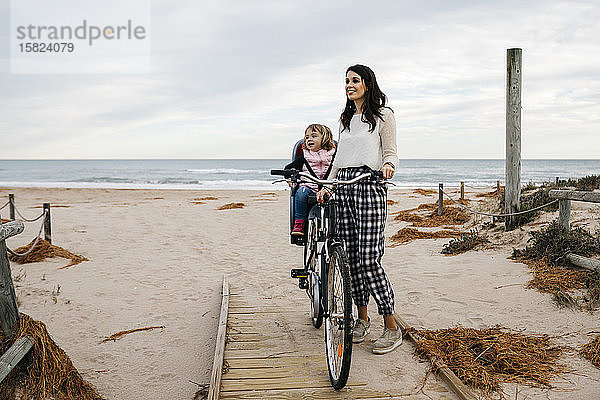 Frau mit Fahrrad auf einer Strandpromenade in den Dünen mit Tochter im Kindersitz