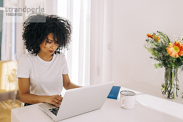 Porträt einer jungen Frau mit lockigem Haar mit Laptop auf dem Tisch zu Hause