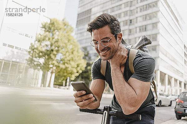 Lässiger Mann mit E-Scooter überprüft Smartphone in der Stadt
