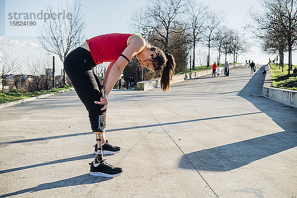 Erschöpfte sportliche junge Frau mit Beinprothese auf einem Gehsteig stehend