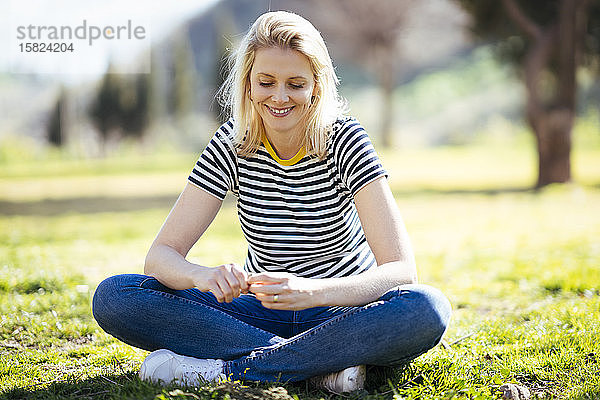 Blond lächelnde Frau sitzt auf einer Wiese in einem Park