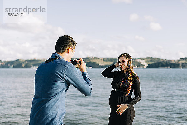 Junger Mann fotografiert seine schwangere Freundin an der Uferpromenade