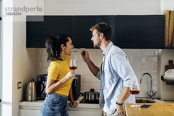 Glückliches junges Paar kocht und trinkt gemeinsam Wein in der heimischen Küche