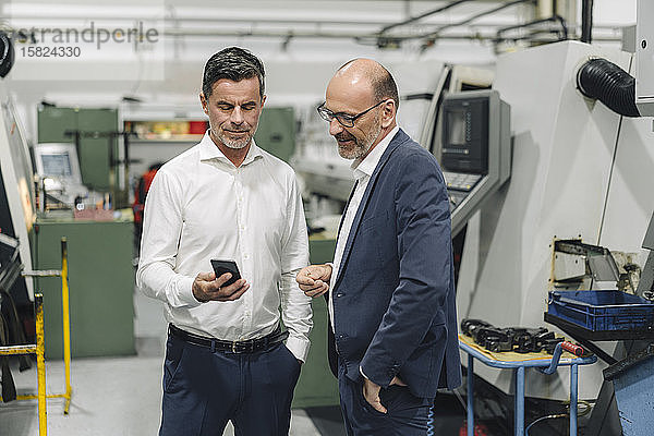 Zwei Geschäftsleute mit Smartphone in einer Fabrik