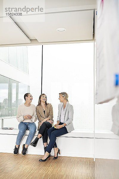 Geschäftsfrauen sitzen auf der Fensterbank im Bürogebäude  machen eine Pause  reden