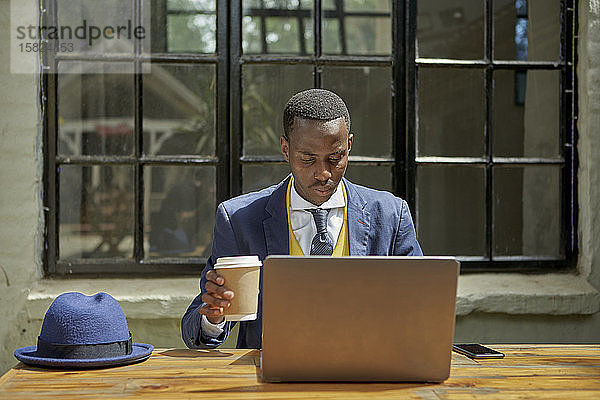 Modischer junger Geschäftsmann im altmodischen Anzug mit Laptop in einem Café im Freien