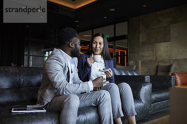 Geschäftsmann und Geschäftsfrau sitzen auf der Couch in der Hotellobby und machen eine Kaffeepause