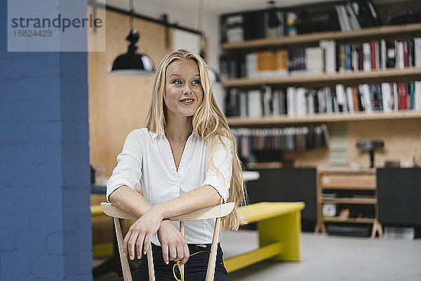 Porträt einer lächelnden jungen Geschäftsfrau  die auf einem Stuhl im Loft-Büro sitzt