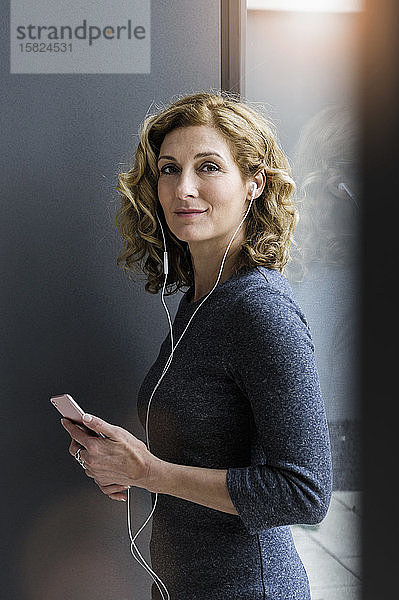Porträt einer blonden Geschäftsfrau mit Kopfhörern und Smartphone im Büro