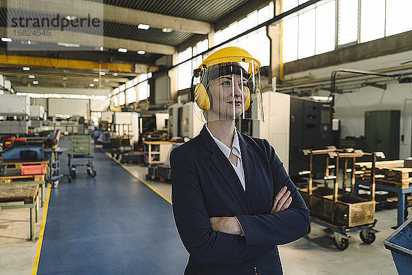 Porträt einer selbstbewussten Geschäftsfrau mit Schutzhelm und Ohrenschützern in einer Fabrik