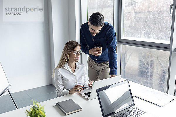 Geschäftsfrau sitzt am Schreibtisch und diskutiert mit ihrem Kollegen über die Arbeit