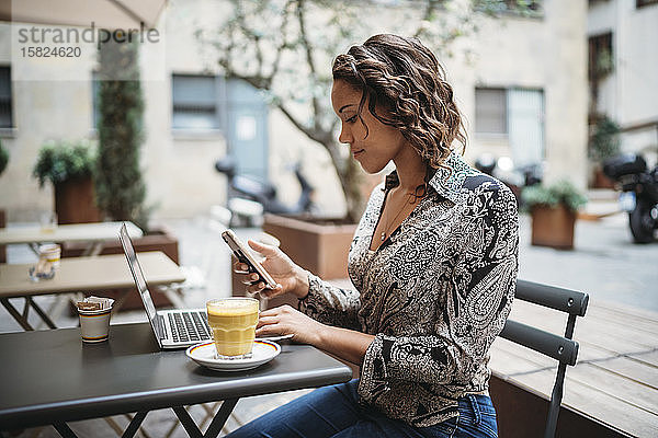 Junge Frau mit Laptop und Smartphone in einem Straßencafé