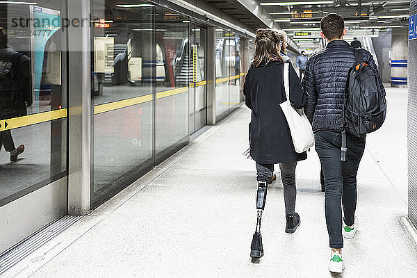 Rückansicht einer jungen Frau mit Beinprothese und eines gehenden Mannes auf dem Bahnsteig einer U-Bahn-Station