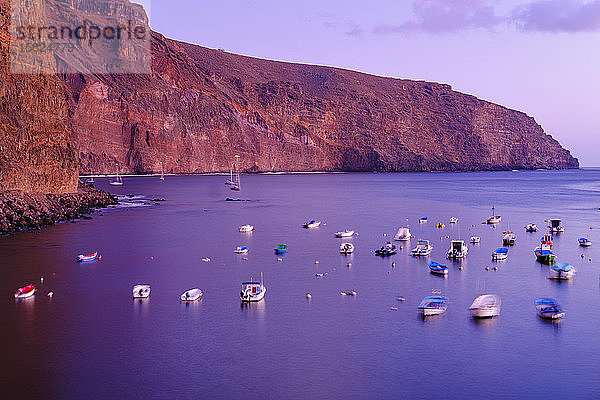 Spanien  La Gomera  Valle Gran Rey  Boote liegen in der violetten Dämmerung vor der Küstenklippe vor Anker