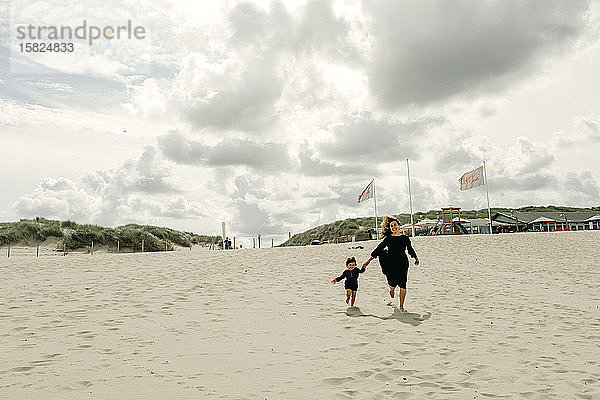 Mutter und kleine Tochter laufen Hand in Hand am Strand  Den Haag  Niederlande