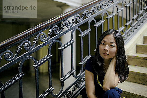 Porträt einer ernsten Frau  die auf einer Treppe in einem alten Gebäude sitzt