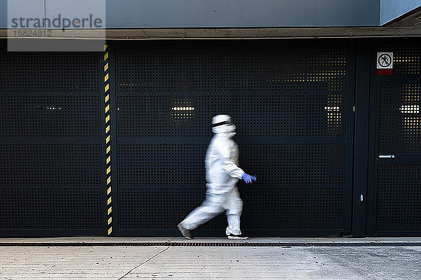 Wissenschaftlerin  die Schutzanzug und Maske trägt und vor einer Wand läuft