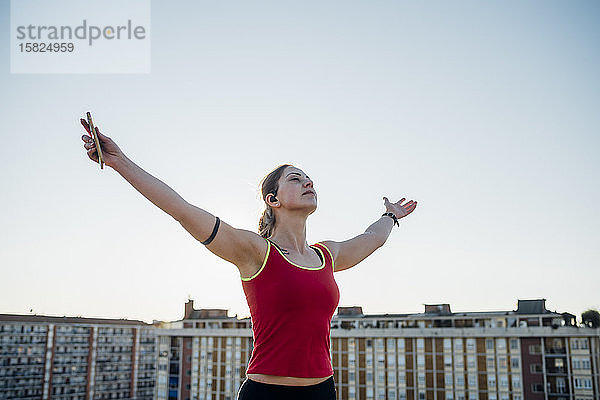 Sportliche junge Frau hebt ihre Arme unter blauem Himmel