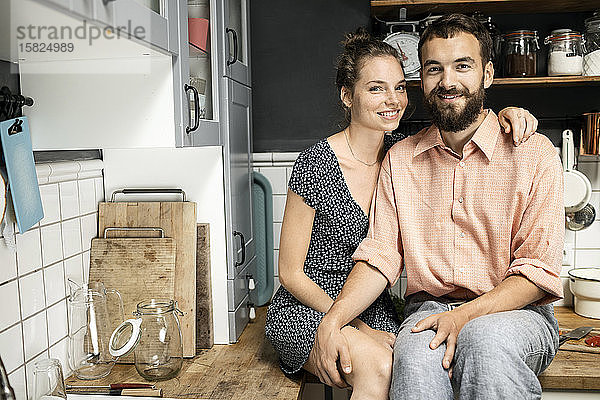 Junges Paar sitzt auf der Küchenarbeitsplatte und lächelt